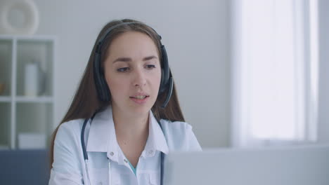 Fleißige-Indische-Ärztin-Führt-Videoanrufe-Auf-Laptop-Im-Krankenhaus-Durch.-Lächelnde-Junge-Ärztin-Trägt-Weißes-Einheitliches-Stethoskop-Und-Berät-Online-Patienten-Per-Videoanruf